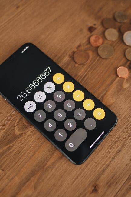 A bright pink calculator with a digital display and white buttons featuring mathematical symbols, placed on an open lined notepad with blank pages. The notepad is positioned on the corner of a desk or